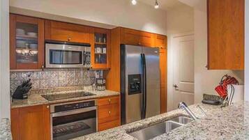 A kitchen with wooden cabinets, a stainless steel refrigerator, a microwave, and a granite countertop.