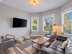 A modern living room with a flat-screen TV mounted on the wall, a sofa, a coffee table, and a floor lamp. - Mississippi Ave Home - Walk to Dining,Shops,Music (Portland)