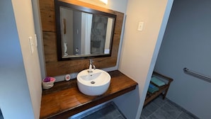 Un baño con tocador de madera, lavamanos blanco, espejo con marco de madera y un perchero para toallas.