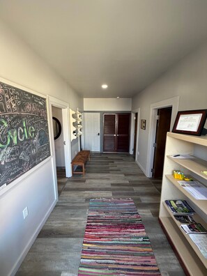 A hallway with a chalkboard on the left, a bench, a colorful rug, and shelves with papers and books.