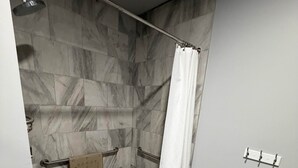 A modern bathroom with a shower, marble tiles, a towel rack, and a shower curtain. - Germantown Inn & Lounge (Hermann)