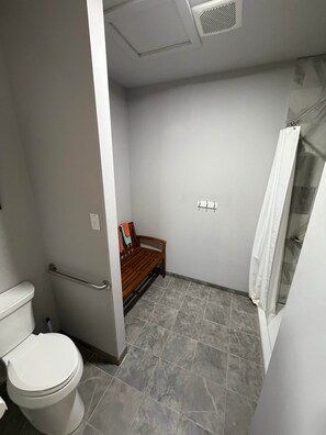 A bathroom with a toilet, a bench, a shower area, and a tiled floor.