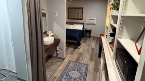 Quarto compacto com cama, mesa de cabeceira e uma pequena janela.