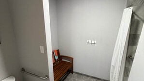 Um banheiro com vaso sanitário, banco e área de chuveiro.