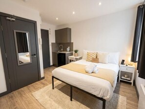 Ett modernt hotellrum med en säng, ett nattduksbord och ett litet pentry.