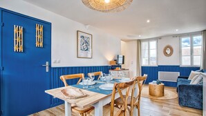 A dining area with a blue door, wooden chairs, a table set for four, and a blue sofa in the background. - L'Escale Bleue - Cosy & Balneo, Village & Sea (Dives-sur-Mer)
