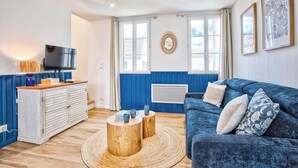 A living room with a blue sofa, wooden coffee table, and a TV on a cabinet. - L'Escale Bleue - Cosy & Balneo, Village & Sea (Dives-sur-Mer)
