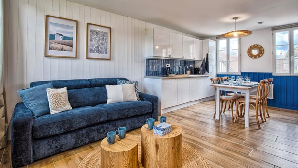 A modern living room with a blue sofa, wooden coffee table, and a dining area with a table and chairs. - L'Escale Bleue - Cosy & Balneo, Village & Sea (Dives-sur-Mer)
