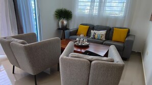 A modern living room with two grey armchairs, a wooden coffee table, and a grey sofa with yellow cushions. - Spacious 3-bedroom apartment in serene Santiago de los Caballeros with AC (Santiago de los Caballeros)