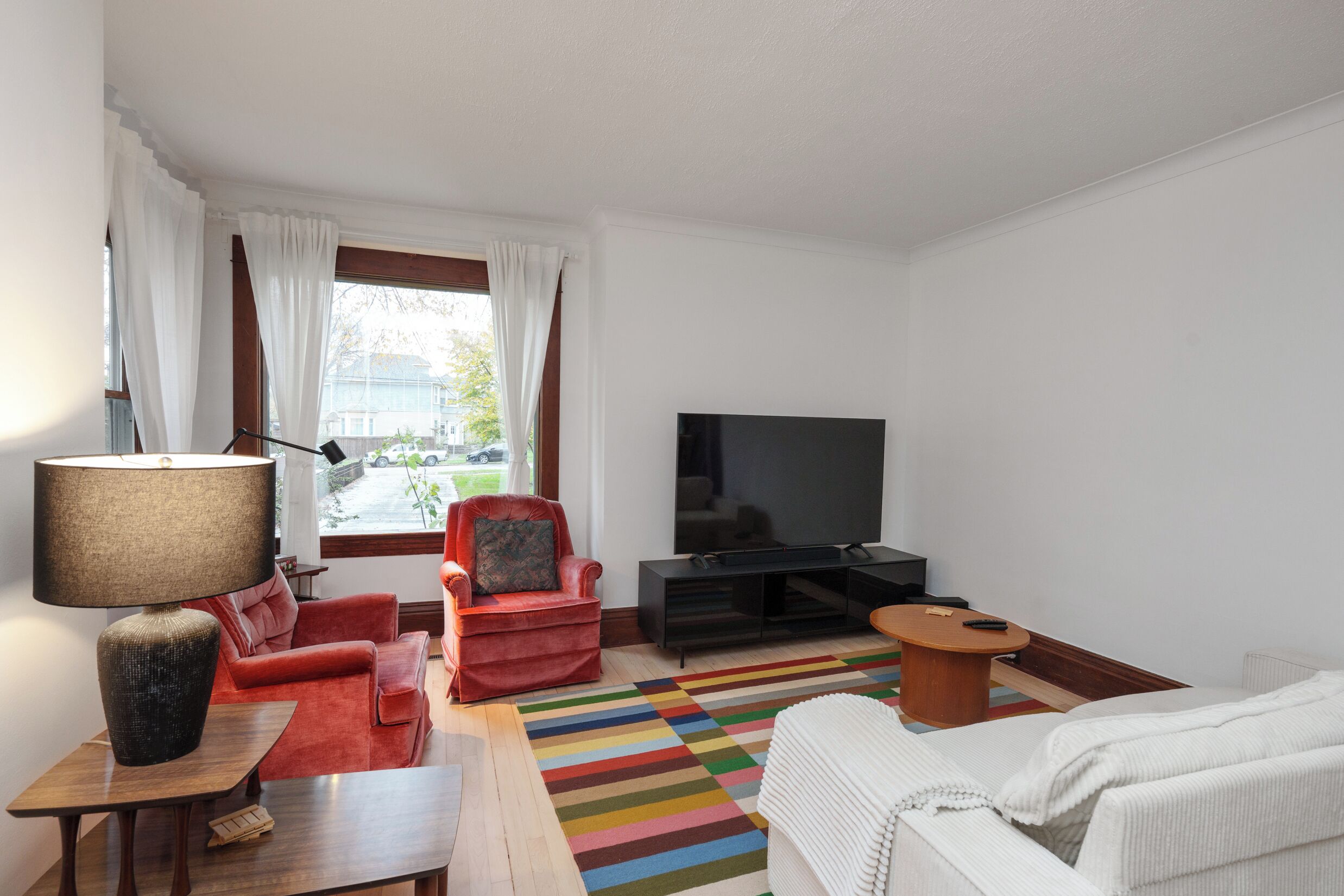 A living room with a TV, red armchair, white sofa, and a striped rug.