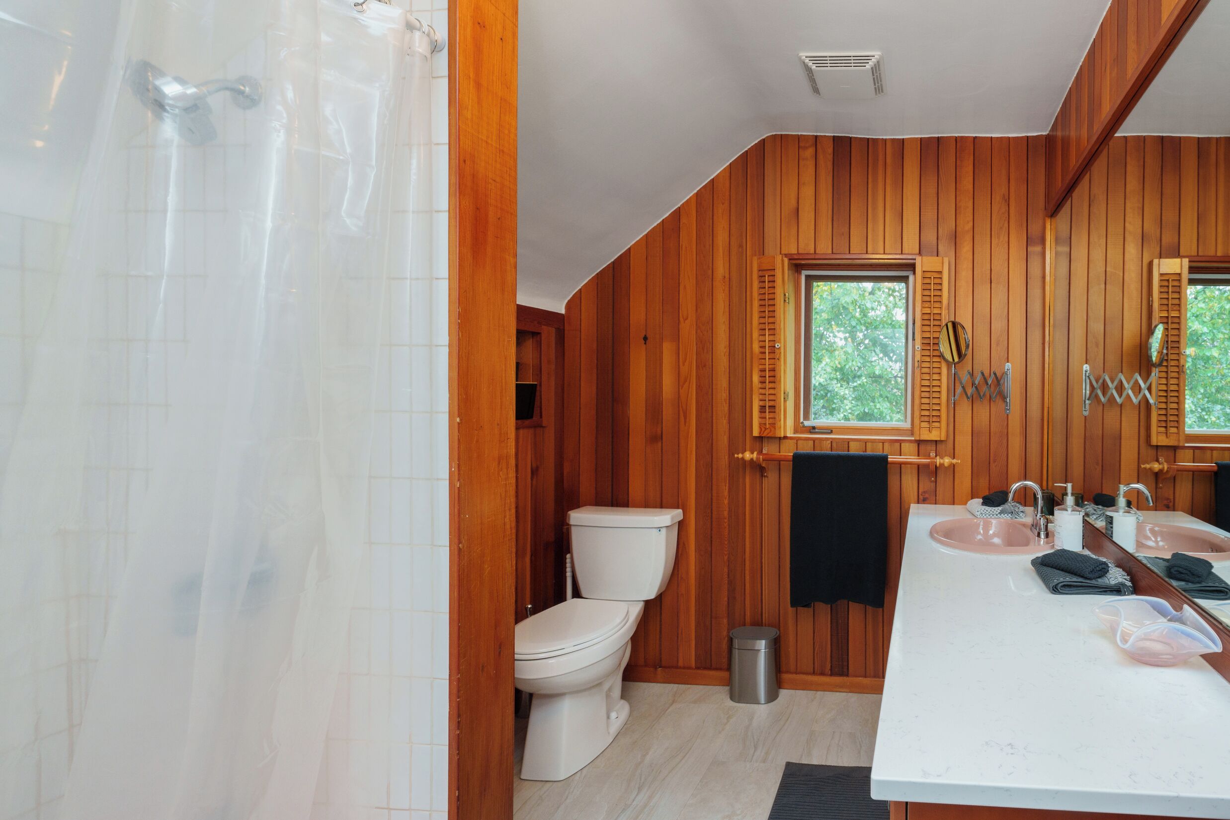 Un bagno con pareti in legno, un WC bianco, un lavandino con specchio e una tenda da doccia.
