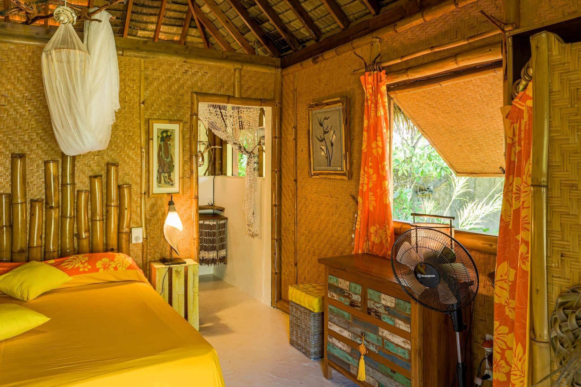Een kamer met een bed, een ventilator, een raam met gordijnen en een deur naar een andere kamer.