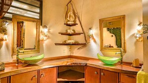 A bathroom with two green ceramic sinks, wooden cabinets, and decorative wall sconces.