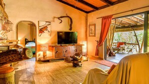 A cozy room with a wooden ceiling, a television, a wooden cabinet, and a large window with a view of the outdoors.