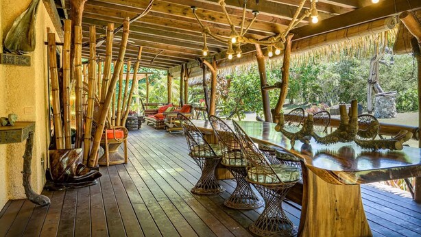 An outdoor wooden deck with bamboo furniture, a glass table, and a ceiling fan.