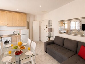 A modern kitchen with white cabinets, a dining area with a glass table, and a grey sofa. - 1 BR Sea View · Steps to Beach · Los Cristianos (Los Cristianos)