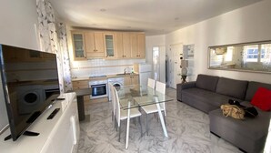 A modern kitchen with marble flooring, a dining area with a glass table, and a living area with a sofa and a television. - 1 BR Sea View · Steps to Beach · Los Cristianos (Los Cristianos)