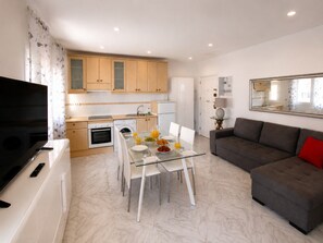A modern living room with a glass dining table, a grey sofa, and a flat-screen TV. - 1 BR Sea View · Steps to Beach · Los Cristianos (Los Cristianos)