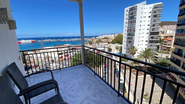 A balcony with a view of the sea, a white building, and a tall residential building. - 1 BR Sea View · Steps to Beach · Los Cristianos (Los Cristianos)