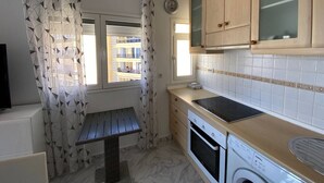 A compact kitchen with a built-in oven, a washing machine, and a window with a view of buildings. - 1 BR Sea View · Steps to Beach · Los Cristianos (Los Cristianos)