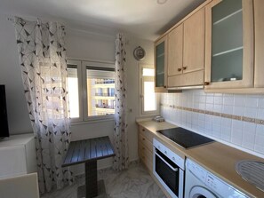 A compact kitchen with a built-in oven, a washing machine, and a window with a view of buildings. - 1 BR Sea View · Steps to Beach · Los Cristianos (Los Cristianos)