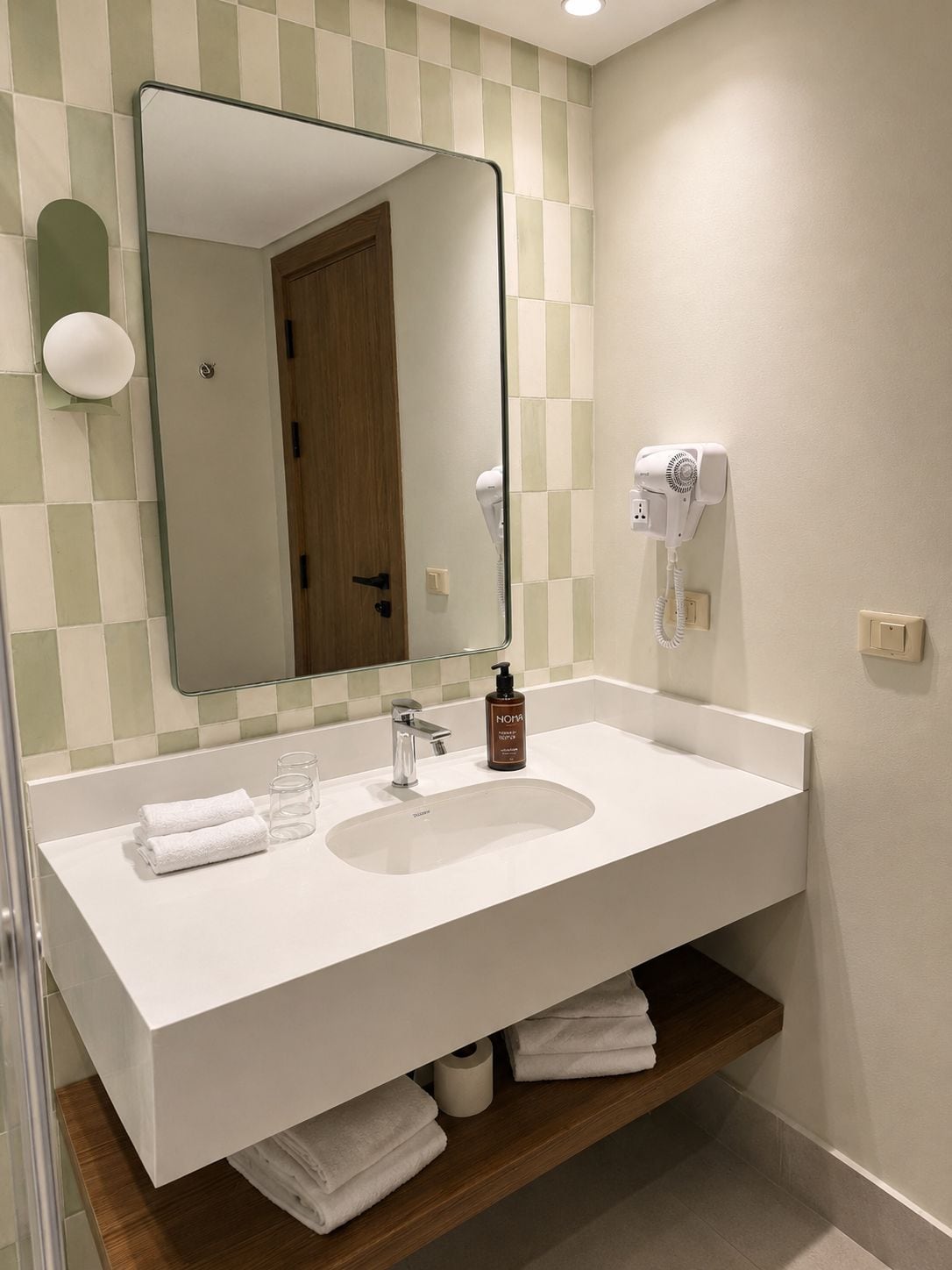 Un baño con lavamanos blanco, un espejo, un secador de pelo y un perchero para toallas.