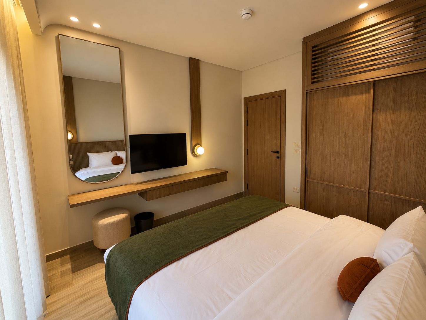 A hotel room with a bed, a television, a mirror, a wardrobe, and a bedside table.