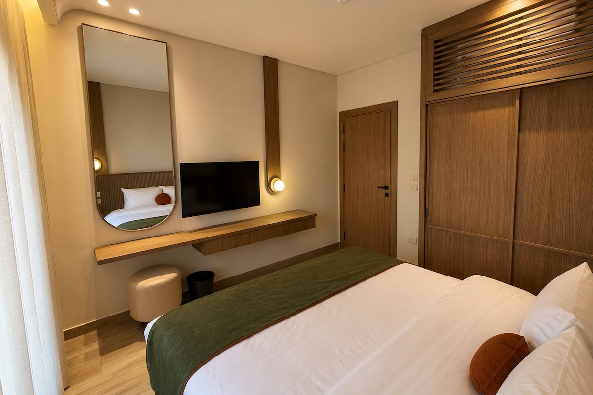 A hotel room with a bed, a television, a mirror, a wardrobe, and a bedside table.