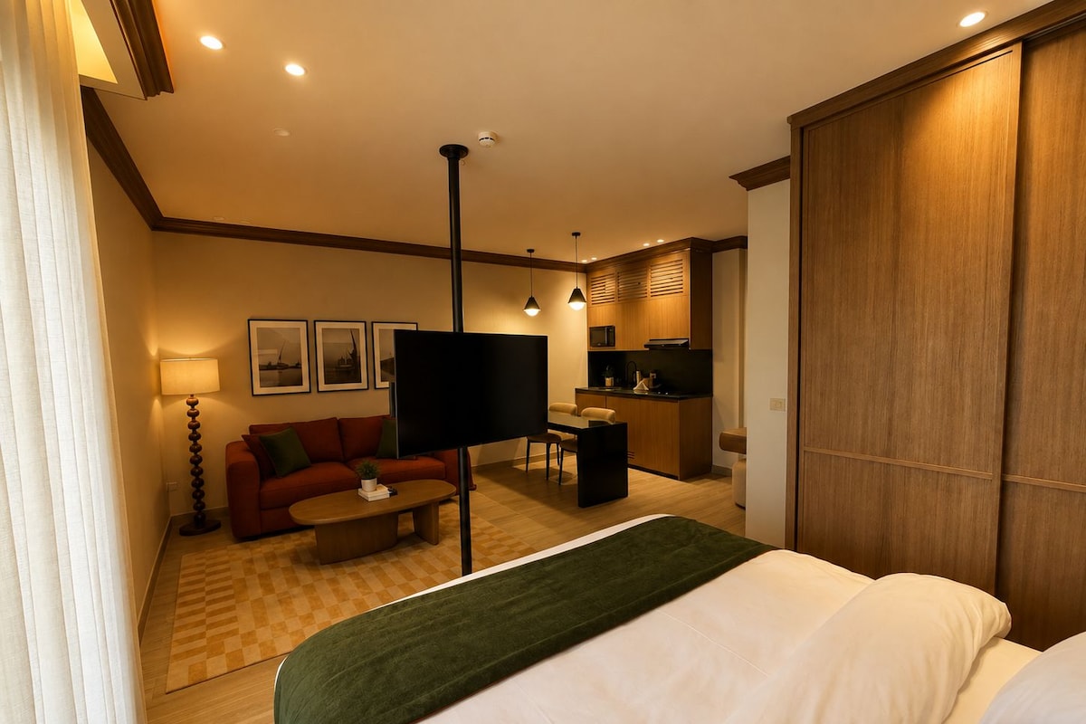 A hotel room with a bed, a sofa, a coffee table, a TV, a desk, and a kitchenette.