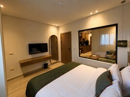 Una habitación de hotel moderna con cama, televisor, espejo y vista a la cocina.