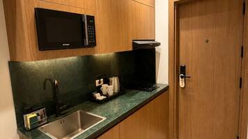Une cuisine compacte équipée d’un four à micro-ondes encastré, d’une machine à café et d’un évier.