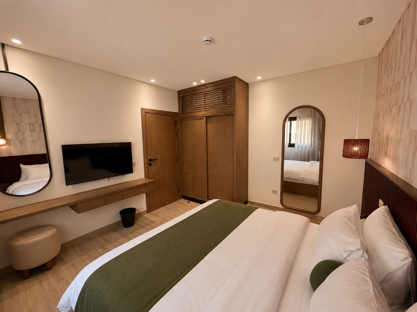 A hotel room with a bed, a TV, a wardrobe, a mirror, and a small stool.