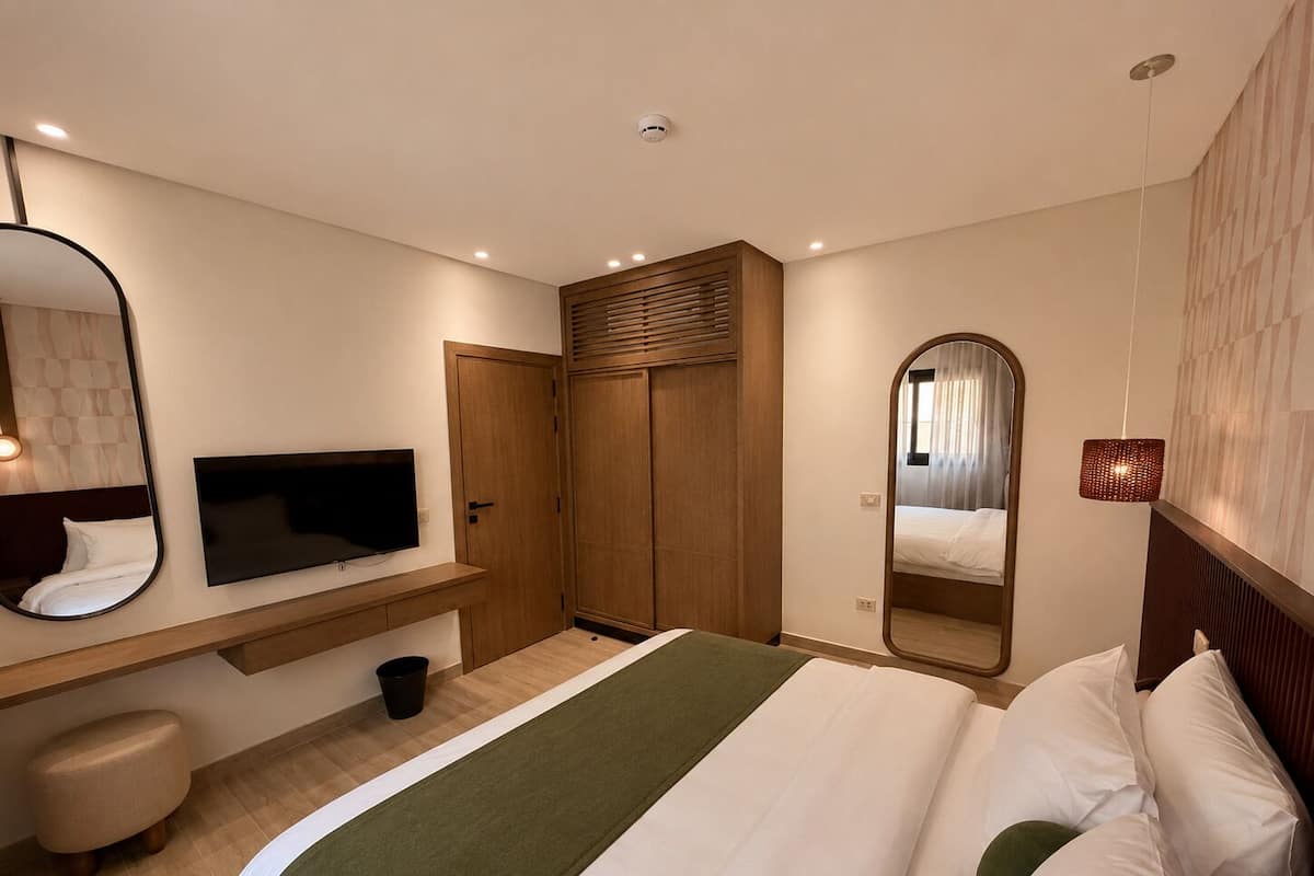 Habitación de hotel con una cama, televisor, armario, espejo y un taburete pequeño.