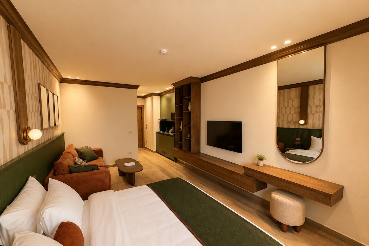 A hotel room with a bed, a sofa, a TV, a mirror, and a small table.