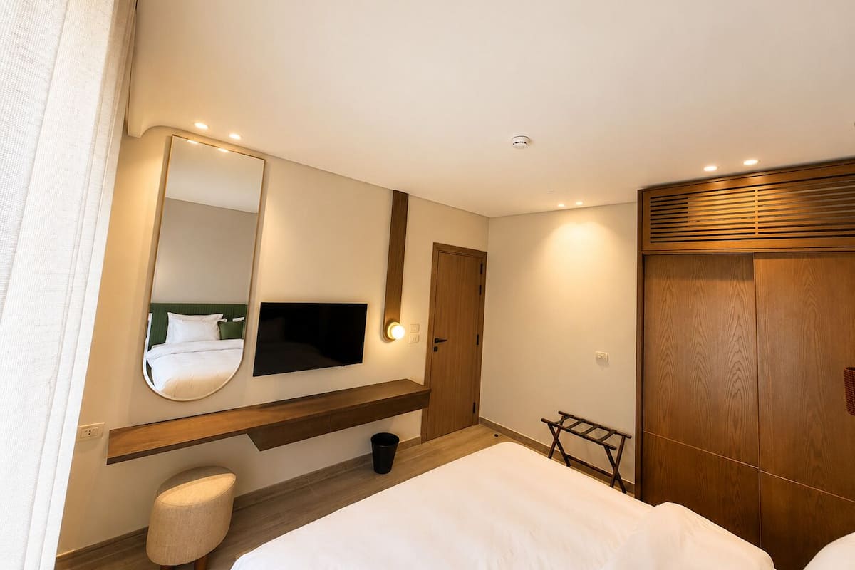 Una habitación de hotel con una cama, un televisor montado en la pared, un armario de madera y un taburete pequeño.
