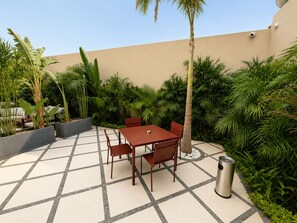 An outdoor patio with a table and chairs, surrounded by lush greenery and a tiled floor. - NOMA New Cairo (New Cairo)