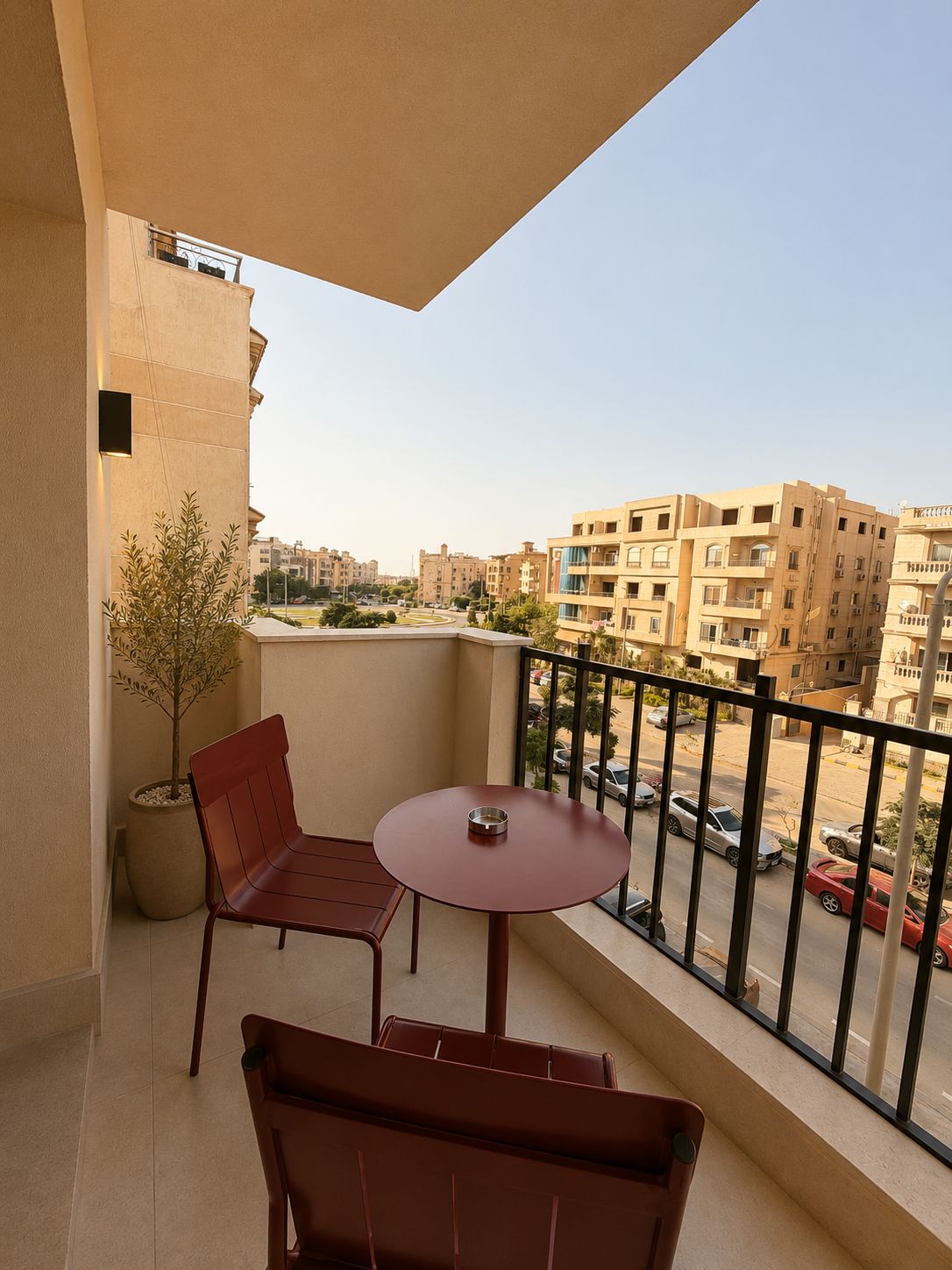 Un balcon avec une table et deux chaises, un pot de fleurs et une vue sur les bâtiments environnants.