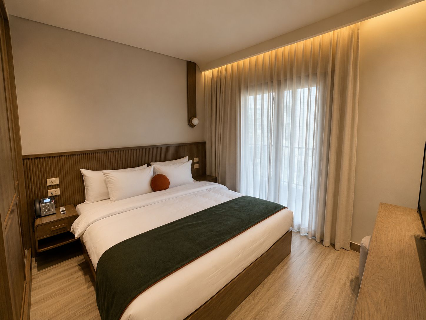Een hotelkamer met een groot bed, een houten hoofdeinde, nachtkastjes met lampen, een flatscreen televisie en een raam met gordijnen.