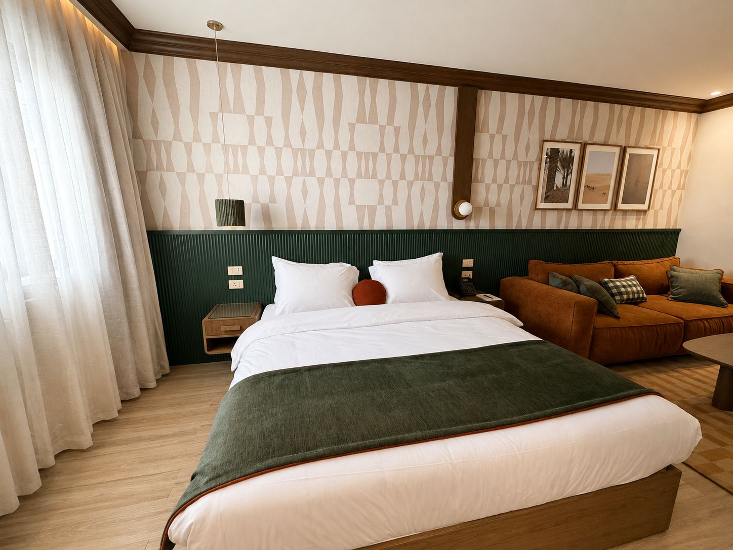 Ein Hotelzimmer mit einem Bett, einem grünen Polsofa, einem hölzernen Nachttisch und einer Wand mit gemustertem Wandpapier.