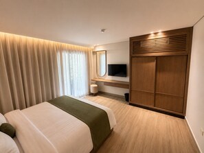 A hotel room with a bed, a TV, a wooden wardrobe, and a window with curtains.
