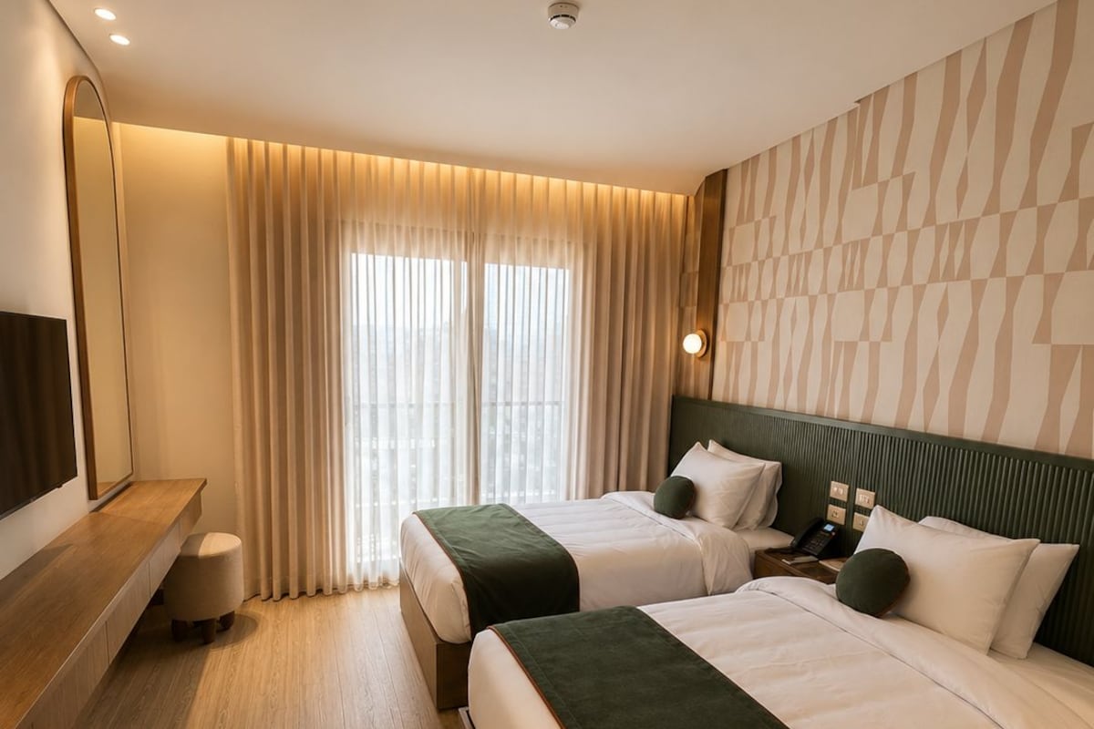 A hotel room with two beds, a flat-screen TV, a bedside table, and a large window with curtains.