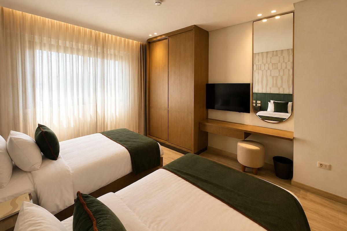 A hotel room with two beds, a TV, a desk, and a mirror.