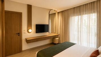A hotel room with a bed, a television mounted on the wall, a wooden door, and a window with curtains.