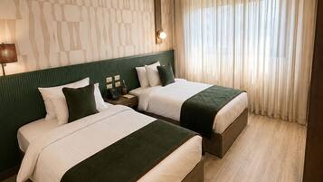 Habitació d'hotel amb dos llits, un mur amb un disseny, una finestra amb cortines i un sòl de fusta.