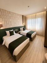 Ett hotellrum med två sängar, en vägg med mönster, ett fönster med gardiner och ett trägolv.
