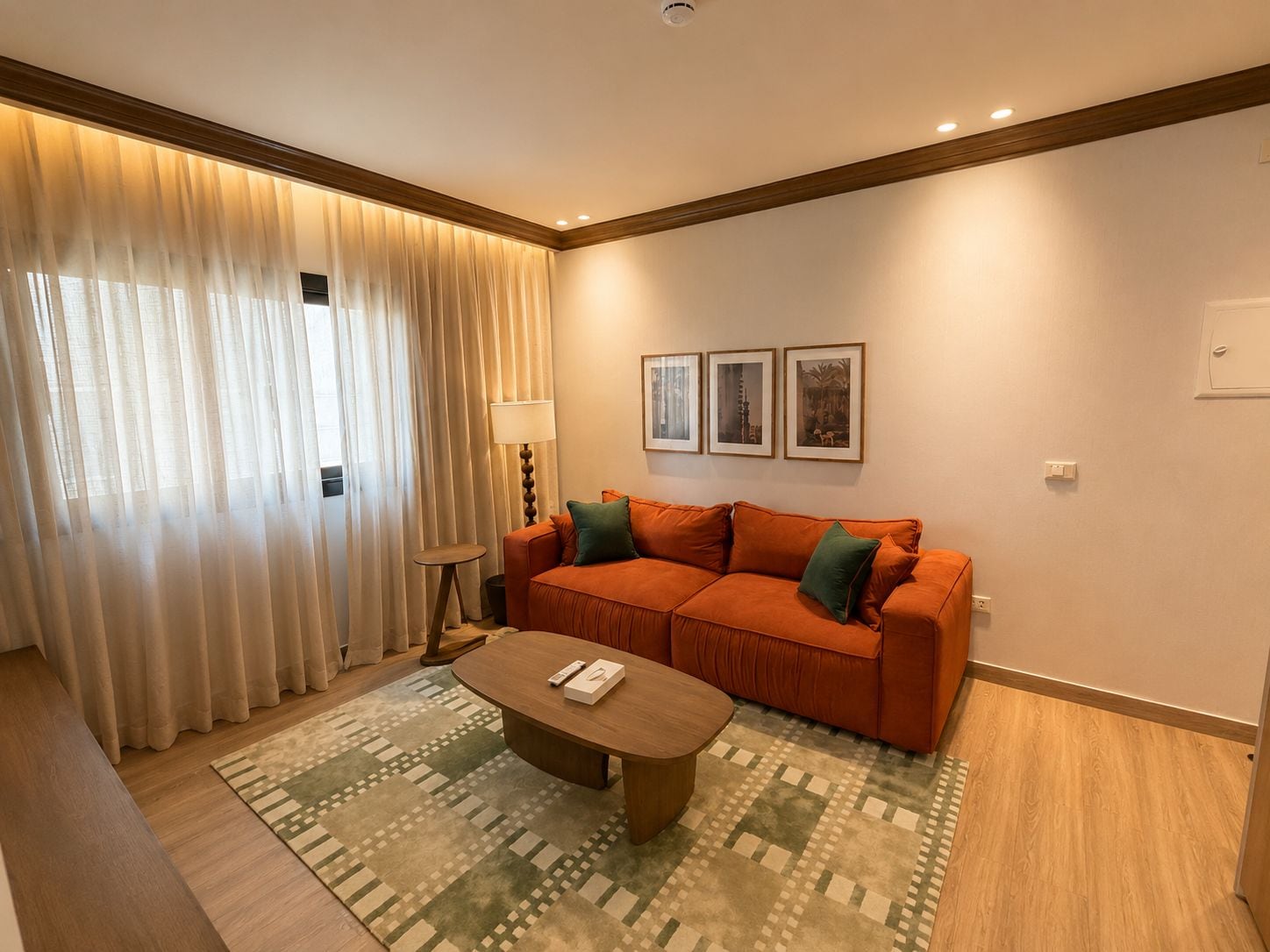 A modern living room with a sofa, a coffee table, and a lamp. There are three framed pictures on the wall.