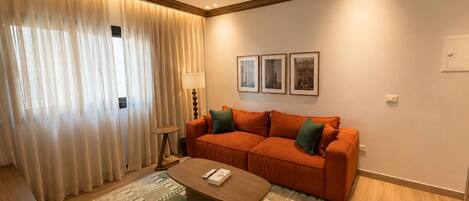 A modern living room with a sofa, a coffee table, and a lamp. There are three framed pictures on the wall.