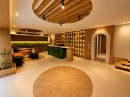 A modern reception area with a wooden reception desk, seating area, and a green wall with shelves.