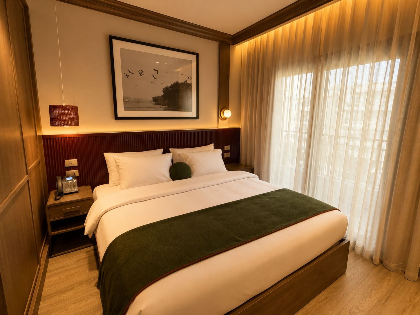 Habitación de hotel con cama, mesita de noche con teléfono, lámpara de pared y ventana con cortinas.