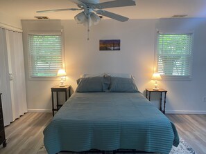 Ein Schlafzimmer mit einem Bett, zwei Nachttischlampen, einem Deckenventilator und zwei Fenstern mit Jalousien.